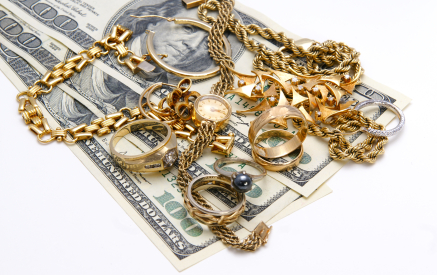Various gold jewelry items sitting atop $100 bills.
