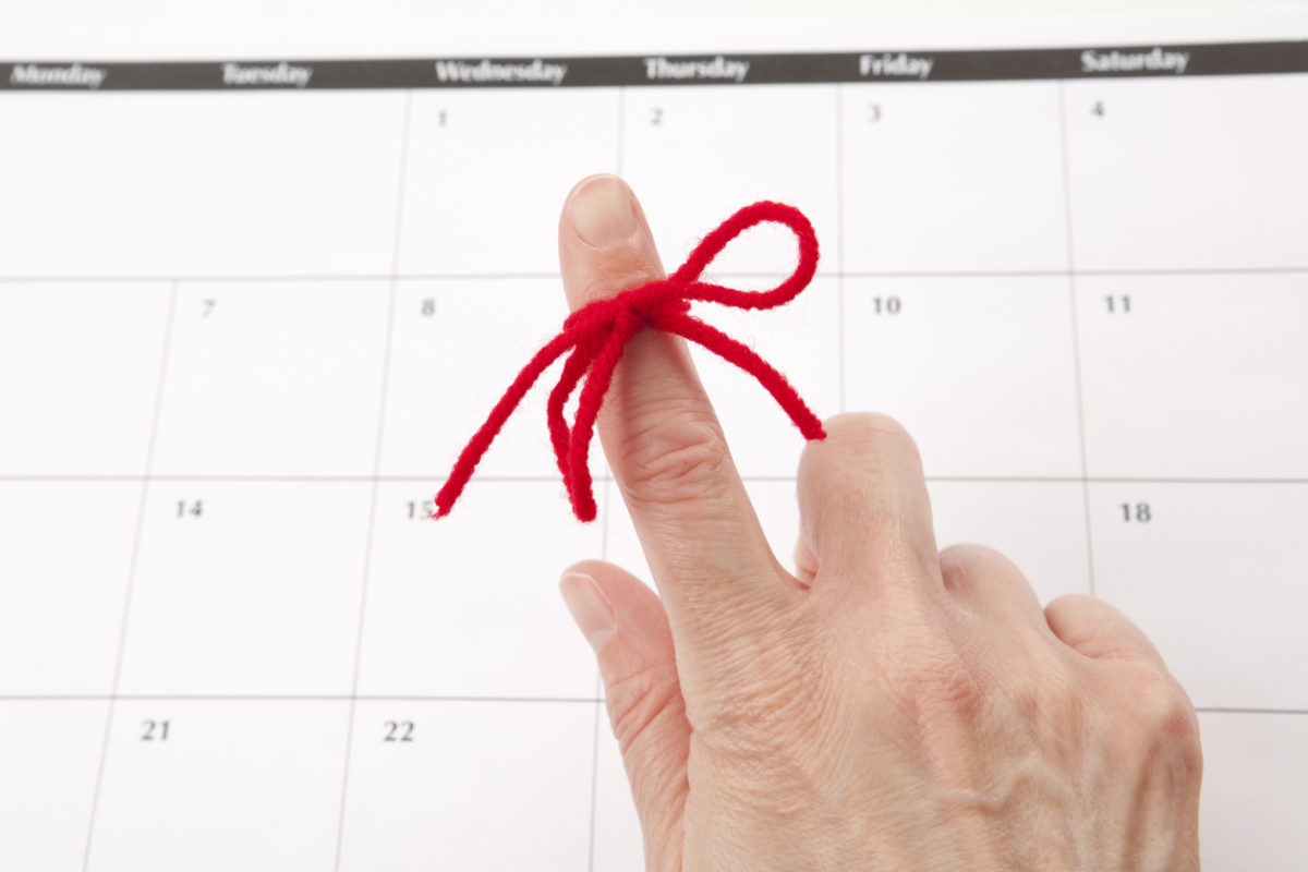 A red string tied around an index finger in front of a calendar: email alerts remind customers when their loans are due