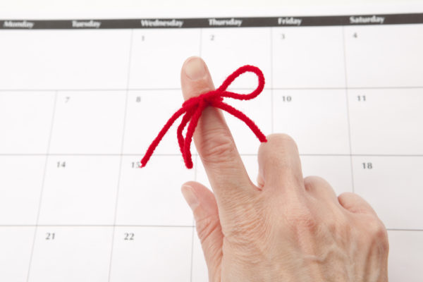 A red string tied around an index finger in front of a calendar: email alerts