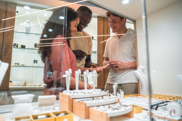 A diverse couple considering various necklaces with the assistance of a Caucasian seller in a jewelry shop.